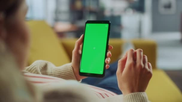 Femme utilisant un smartphone avec écran vert dans le salon — Video