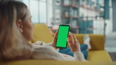 Oturma odasında yeşil ekranlı akıllı telefon kullanan kadın.