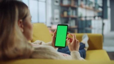 Oturma odasında yeşil ekranlı akıllı telefon kullanan kadın.