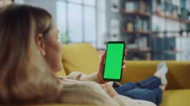 Oturma odasında yeşil ekranlı akıllı telefon kullanan kadın.