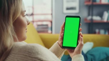 Oturma odasında yeşil ekranlı akıllı telefon kullanan kadın.
