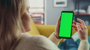 Oturma odasında yeşil ekranlı akıllı telefon kullanan kadın.
