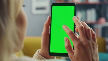 Oturma odasında yeşil ekranlı akıllı telefon kullanan kadın.