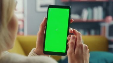 Oturma odasında yeşil ekranlı akıllı telefon kullanan kadın.