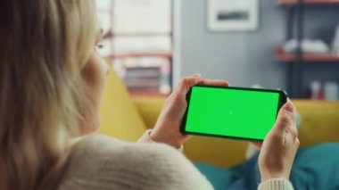 Oturma odasında yeşil ekranlı akıllı telefon kullanan kadın.