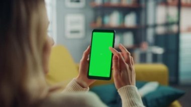 Oturma odasında yeşil ekranlı akıllı telefon kullanan kadın.