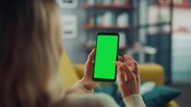 Oturma odasında yeşil ekranlı akıllı telefon kullanan kadın.