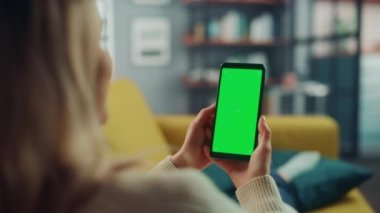 Oturma odasında yeşil ekranlı akıllı telefon kullanan kadın.