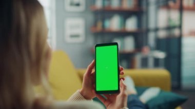 Oturma odasında yeşil ekranlı akıllı telefon kullanan kadın.