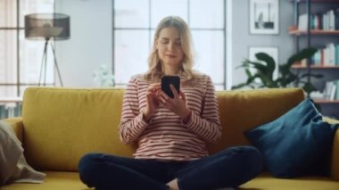 Akıllı telefonlu bir kadın oturma odasında, koltukta oturuyor.