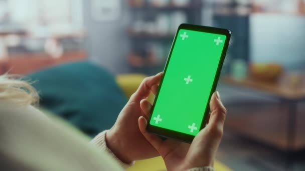 Женщина с помощью смартфона с зеленым экраном в гостиной — стоковое видео
