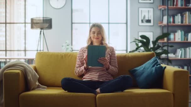 Mujer con la tableta sentada en el sofá en la sala de estar — Vídeos de Stock