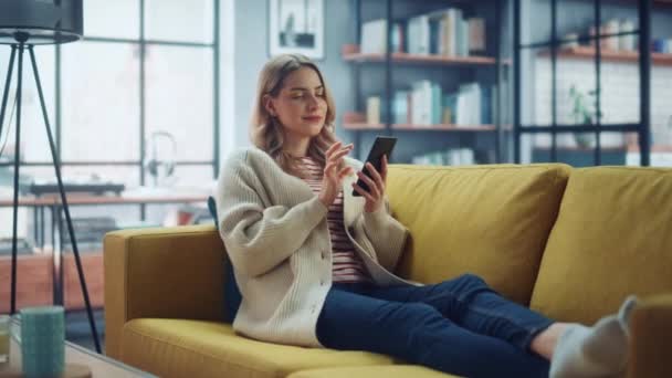 Женщина со смартфоном отдыхает на диване в гостиной — стоковое видео