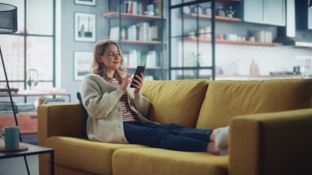 Γυναίκα με Smartphone Ξεκούραση στον καναπέ στο σαλόνι — Αρχείο Βίντεο