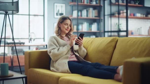 Женщина со смартфоном отдыхает на диване в гостиной — стоковое видео