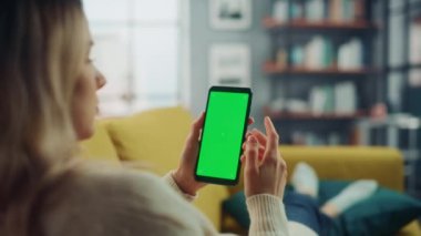 Oturma odasında yeşil ekranlı akıllı telefon kullanan kadın.