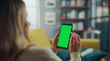 Oturma odasında yeşil ekranlı akıllı telefon kullanan kadın.