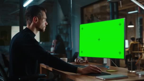 男はクリエイティブオフィスで緑の画面を持つコンピュータ上で動作します — ストック動画