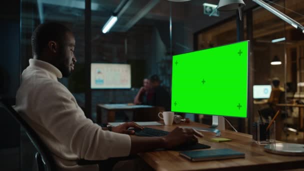 El hombre negro trabaja en la computadora con pantalla verde en la oficina creativa — Vídeo de stock