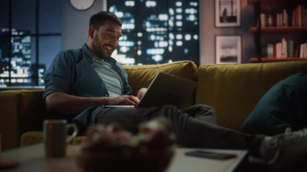 Мужчина с ноутбуком отдыхает в темной гостиной в вечернее время — стоковое видео