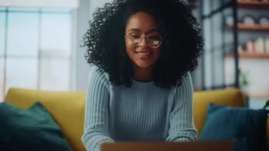 Dizüstü bilgisayarlı bir kadın oturma odasında, koltukta oturuyor.