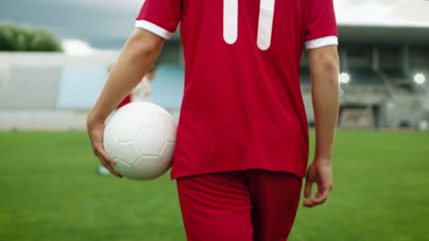 Fotbollsspelare går med en boll under armen på fältet där lagkamrater utbildning — Stockvideo