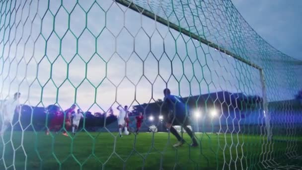 Detrás de la red de tiro portero de fútbol de pie en las metas tratando de atrapar la pelota pateada por atacar al equipo, pero fallando — Vídeos de Stock