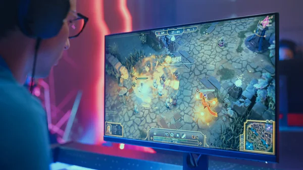 Профессиональный eSports Gamer играет RPG MOBA макет видео игры с супер действия и забавные специальные эффекты на своем персональном компьютере, разговаривает с товарищами по команде с помощью гарнитуры. Стильный ретро-неоновый зал для киберигр — стоковое фото
