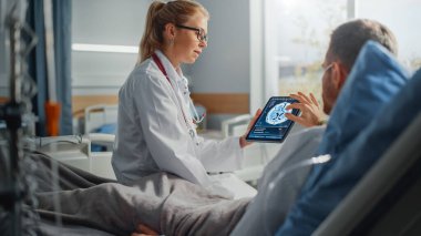 Hastane Koğuşu: Dost Canlısı Kadın Doktor Hasta Hasta Hasta ile Konuşuyor, Tablet Bilgisayar Kullanıyor, Beyin Taraması Sonuçlarını Açıklıyor. Doktor, ameliyattan sonra iyileşen bir adamla konuşuyor.