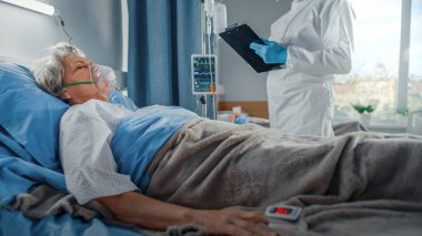 Coronavirus Hastanesi Acil Servisi: Yatakta Oksijen Maskeli Yaşlı Bir Kadın Hastanın Hayati bulgularını Kapsayan Kapalı Giysi Giyen Doktor. Sağlık görevlileri, sağlık görevlileri hayat kurtarmak için her şeyi yapıyor.