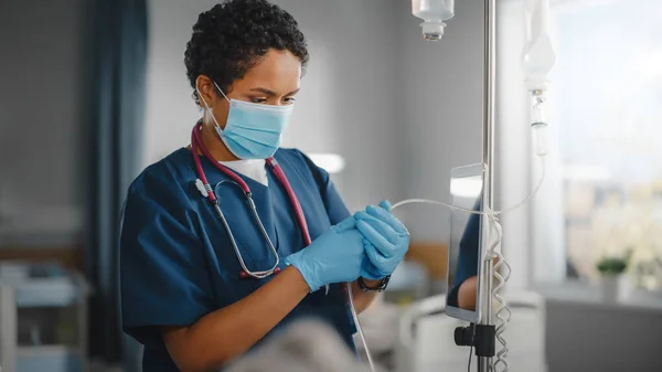 Hospital Ward: Professional Black Head Nurse Wearing Face Mask Does Checkup of Patients Vitals, Checking Heart Rate Computer, Intravenous or Iv Fluids Drip Bag. Caring Nurse Monitors Person Recovery