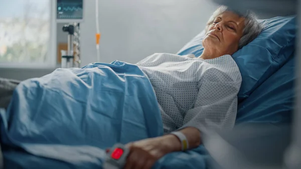 Ziekenhuisafdeling: Senior Woman rustend in een bed met Finger Heart Rate Monitor Pulsoximeter die Puls toont. Haar fragiele handen rusten op een deken. Focus op de Hand. — Stockfoto