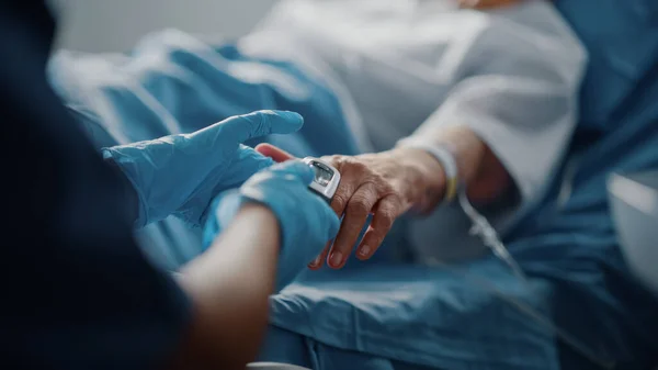 Oddział szpitalny: Starsza kobieta odpoczywająca w łóżku pielęgniarka ma Finger Pulsometr Pulsoksymetr pokazuje puls. Anonimowa pielęgniarka sprawdza funkcje życiowe kobiety Zdrowieje po operacji. — Zdjęcie stockowe