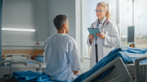 Hospital Ward: Sentado na cama Caucasiano Paciente do sexo masculino ouve experiente médico feminino explicando resultados do teste, dá conselhos, usado Tablet Computer. Homem recuperando após a cirurgia bem sucedida, doença — Fotografia de Stock