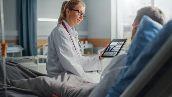 Hospital Ward: Amigável Médica Feminina Fala com Doente Paciente Masculino Descansando na Cama, Usa Tablet Computer, Mostra e Explica os Resultados da Escaneamento Pulmonar. Médico conversa com um homem recuperando após a cirurgia — Fotografia de Stock