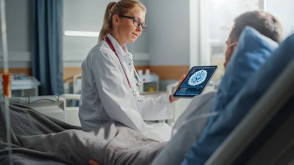 Hospital Ward: Vänliga kvinnliga läkare samtalar med sjuka manliga patienten vilar i sängen, använder Tablet Computer, visar och förklarar hjärnskanning resultat. Läkaren pratar med en man som tillfrisknar efter operationen — Stockfoto