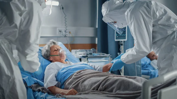 Servicio de Urgencias del Coronavirus Hospitalario: Equipo de Médicos vistiendo Coveralls, Mascarillas para la Cara Cuidar a un Paciente Mayor acostado en la cama, Poner Máscara de Oxígeno y Conectar Goteo Iv. Médicos salvando vidas —  Fotos de Stock