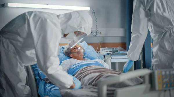病院コロナウイルス緊急部病棟:医師,カバーを身に着けている救急車,顔のマスク酸素マスクでベッドに横たわっている高齢女性患者の命を救う,接続IV,心拍数センサー — ストック写真
