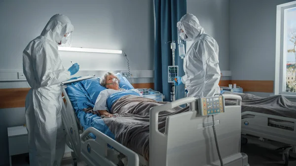 Coronavirus Emergency Department Ward: Doctors, Paramenters wearing Coveralls, Face Mask Save Life of a senior Female Patient Lying in Bed with Oxygen Mask, Connect Iv Drip, Heart Rate Sensor — 스톡 사진