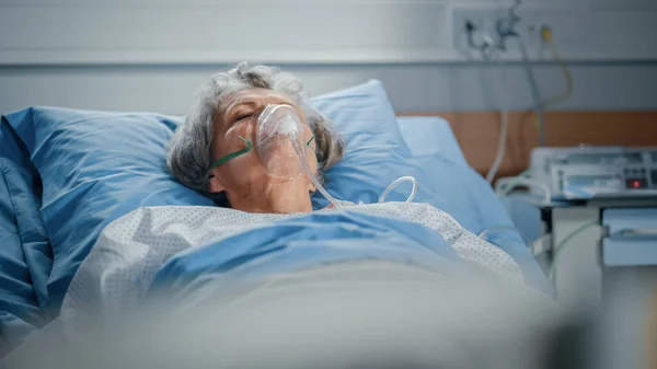 Hospital Ward: Portret van mooie oudere vrouw dragen zuurstofmasker Slapen in bed, volledig herstellen na ziekte. Oude dame droomt van haar familie, vrienden, gelukkig leven. — Stockfoto