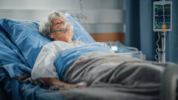 Oddział szpitalny: Portret pięknej starszej kobiety noszącej maskę tlenową śpiącej w łóżku, w pełni zdrowiejącej po chorobie. Staruszka marzy o swojej rodzinie, przyjaciołach, szczęśliwym życiu. — Zdjęcie stockowe