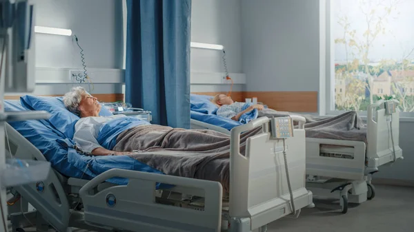 Hospital Ward: Oudere oude dame en jong mooi meisje rusten in bedden, volledig herstellen van succesvolle chirurgische ingrepen. Patiënten herstellen de gezondheid na ziekte. Moderne kliniek met zonnig raamzicht — Stockfoto