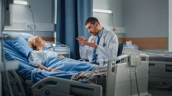 Hospital Ward: Amistosa doctora habla con una joven sonriente que descansa en la cama, recuperándose completamente después de una enfermedad. Médico utiliza Tablet Computer, hace chequeo, da consejos de tratamiento, Recomendación de salud —  Fotos de Stock