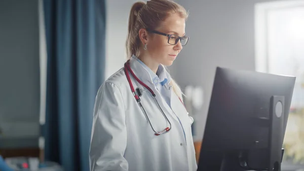 Hospital Ward : Médecin souriant professionnel de race blanche portant une blouse de laboratoire et un stéthoscope utilise un ordinateur d'équipement médical. Patients dans les lits se rétablissant avec succès après une maladie, une chirurgie — Photo