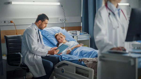 Hospital Ward: Professional Female Doctor Uses Medical Computer (en inglés). En el fondo Equipo moderno Cirujano de la clínica utilizando Tablet Computer Consulting Paciente Recuperación después de una cirugía exitosa en la cama —  Fotos de Stock