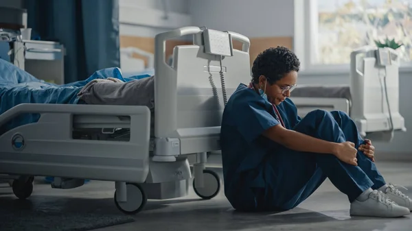 병원 내의 Intensive care Coronavirus Ward: Portrait of Sad, Tired Black Nurse Wearing Face Mask sitting on a Floor, Sorry for All the Patients Lost to Pandemic. 용감 한 영웅 구조 대원들 이 생명을 구하다 — 스톡 사진