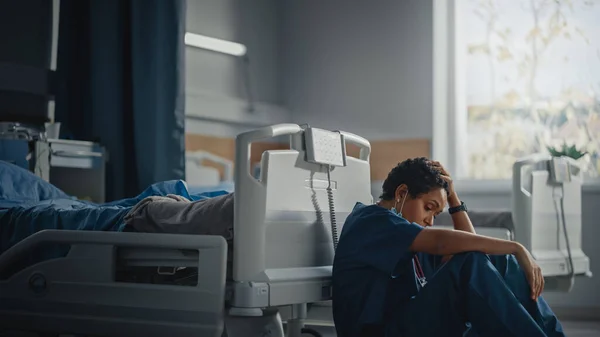 병원 내의 Intensive care Coronavirus Ward: Portrait of Sad, Tired Black Nurse taking off Face Mask sitting on a Floor, Sorry for All the Patients Lost to Pandemic. 용감 한 영웅 구조 대원들 이 생명을 구하다 — 스톡 사진