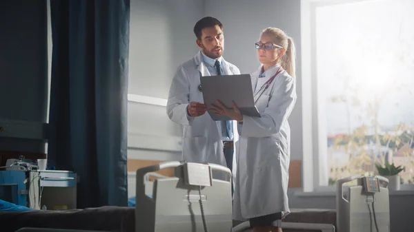 Hospital Ward: Male and Feamle Professional Doctors Hold Laptop Computer, Talk About Patient Medical History, Discuss Health Care Advice, Treatment Plan. Modern Clinic with Advanced Equipment — Stock Photo, Image