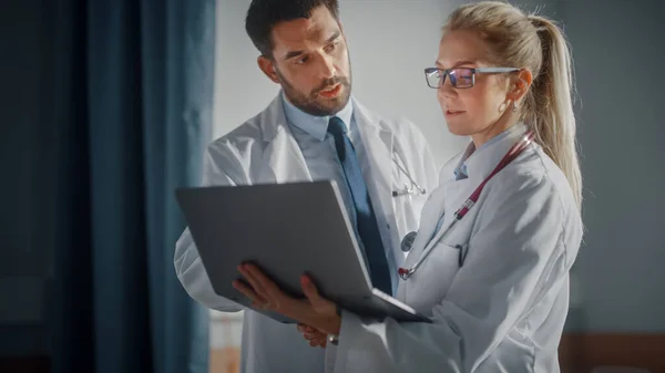 Krankenhausstation: Männliche und weibliche professionelle Ärzte halten Laptop-Computer, sprechen über die Krankengeschichte des Patienten, besprechen Gesundheitsberatung, Behandlungsplan. Moderne Klinik mit moderner Ausstattung — Stockfoto