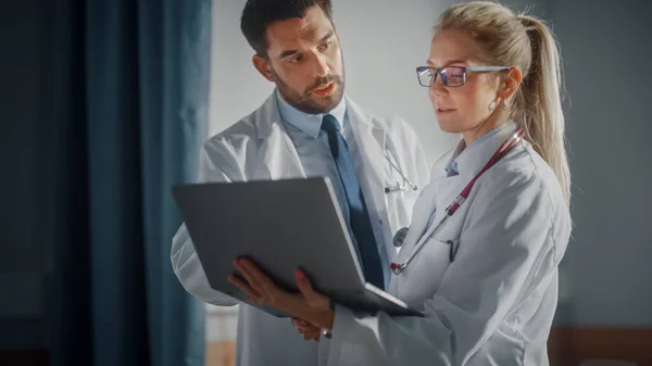 Hospital Ward: Male and Feamle Professional Doctors Hold Laptop Computer, Talk About Patient Medical History, Discuss Health Care Advice, Treatment Plan. Modern Clinic with Advanced Equipment — Stock Photo, Image